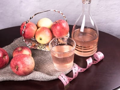 Ein Glas und eine Flasche Apfelessig mit einem Maßband und frischen Äpfeln auf dem Tisch