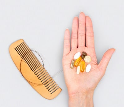 Biotin-Tabletten gegen Haarausfall und ein Kamm mit ausgefallenen Haaren