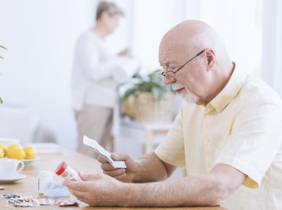 Ein älterer Mann liest eine Packungsbeilage für ein cholesterinsenkendes Medikament.