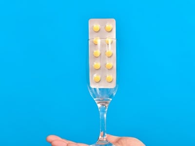 Ein Mann h&auml;lt ein Champagnerglas mit gelben Pillen in der Hand.