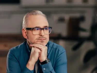 Ein nachdenklicher, älterer Mann mit Brille stützt sein Kinn auf die Hände
