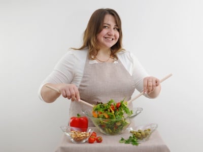 Eine lächelnde Frau in einer Schürze hält eine Salatschüssel.