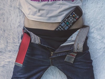 Ein Mann liegt im Bett mit der Fernbedienung des Fernsehers in seiner Unterhose.