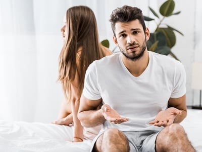 Ein junger, frustrierter Mann mit Ejakulationsproblemen sitzt neben seiner Freundin auf dem Bett.