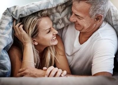 Um casal maduro a fazer amor e a sorrir na cama.