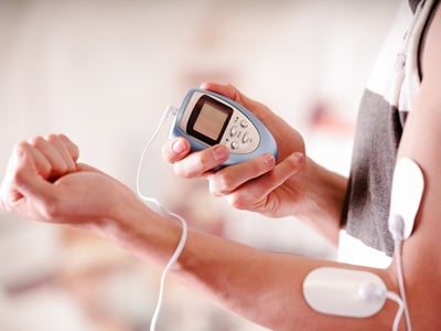 Ein Mann hält ein Elektrostimulationsgerät in der Hand und hat Elektroden in seinem Arm