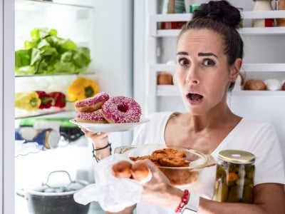 Eine Frau in einem Essanfall nimmt eine Menge Lebensmittel aus dem Kühlschrank