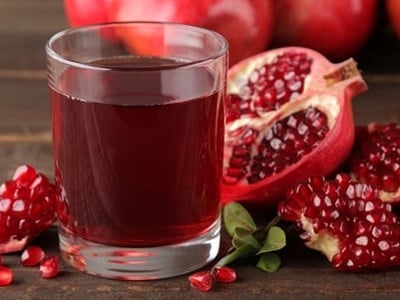 Granatapfelsaft in einem Glas und frische Granatäpfel drum herum