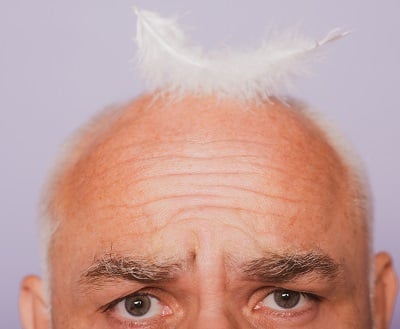 Ein älterer Mann mit einer Feder auf dem kahlen Kopf als ein Symbol für Haarausfall im Alter.