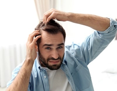 Ein Mann bemerkt Anzeichen von Haarausfall und Glatzenbildung.