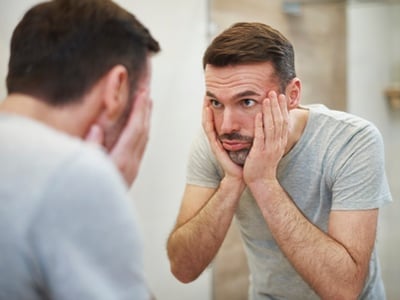 Ein gestresster Mann, der müde und deprimiert in den Spiegel schaut