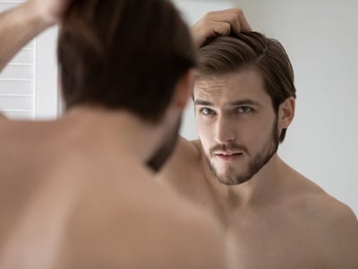 Ein Mann, der sich wegen seines Haarausfalls besorgt im Spiegel betrachtet