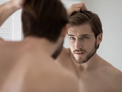 Ein Mann schaut besorgt wegen seines Haarausfalls in den Spiegel