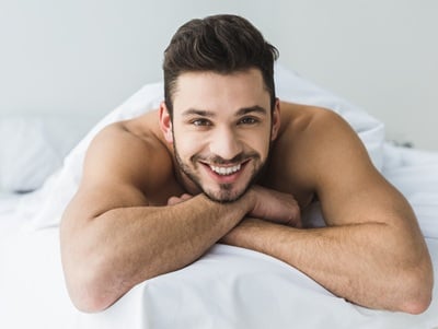Ein gutaussehender, lächelnder Mann, der auf dem Bett liegt und mit sich selbst zufrieden ist.