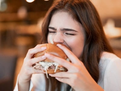  Eine junge Frau isst einen Burger, weil sie einen Heißhungeranfall hat