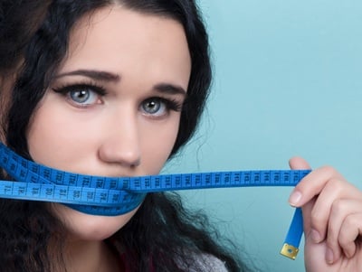 Eine junge Frau mit einem blauen Maßband über dem Mund