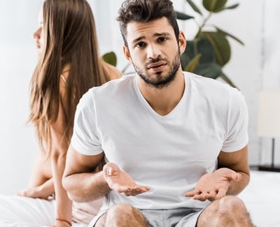 Ein junger frustrierter Mann hat sexuelle Probleme, während er auf dem Bett neben seiner Freundin sitzt