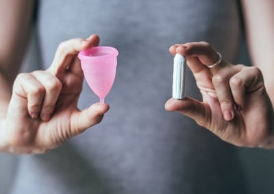 Junge Frauenhände halten verschiedene Arten von Damenhygieneprodukten - Menstruationstasse und Tampon