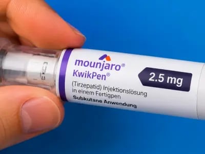 Person hält einen Mounjaro KwikPen (2,5 mg) vor blauem Hintergrund