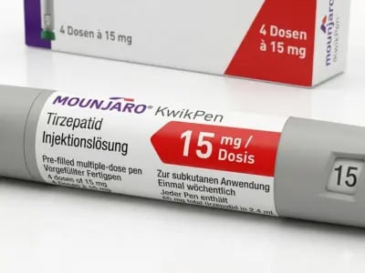 Nahaufnahme eines grauen Mounjaro KwikPens für 15 mg/Dosis mit deutscher Beschriftung auf einem weißen Tisch, mit einer passenden Verpackung im Hintergrund.