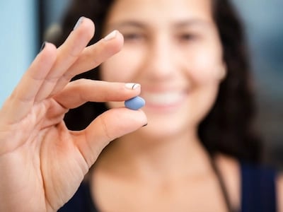 Mulher a segurar um comprimido de Viagra com o dedo indicador e o polegar