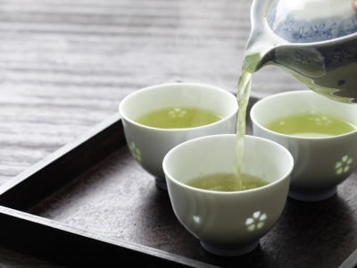 Grüner Tee aus einer Teekanne in Tassen gießen