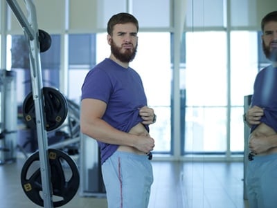 Ein Mann ist wegen seines dicken Bauches nach dem Training enttäuscht.