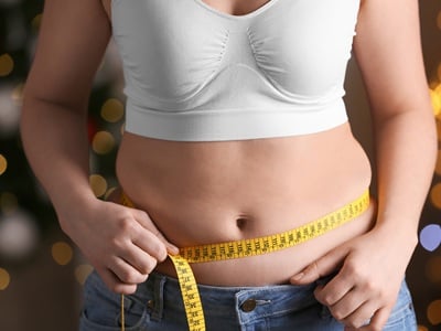 Eine Frau misst ihre Taille mit einem gelben Maßband.