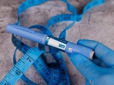 En hånd med blå handsker præsenterer en Ozempic-pen og et målebånd