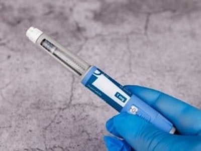 Hånd med blå handsker holder semaglutid-pen