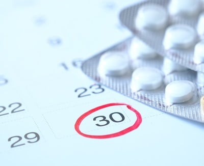 Pillen und ein Kalender mit einem eingekreisten Datum auf dem Tisch