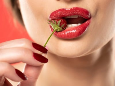 Eine Frau mit roten Lippen und Nägeln hält eine Erdbeere.