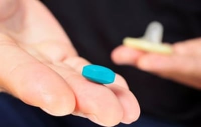 Ein Mann hält eine blaue Pille in der einen und ein Kondom in der anderen Hand.