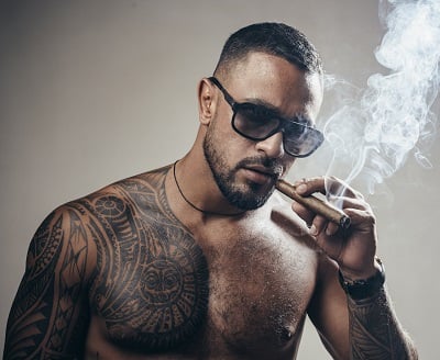 Ein gut aussehender, muskulöser Mann raucht eine Zigarre.