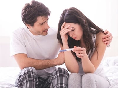 Ein besorgter Mann, der seine depressive Frau mit einem negativen Schwangerschaftstest tröstet