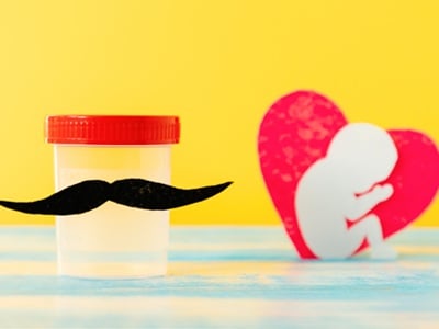 Reagenzglas mit Sperma, Filzschnurrbart und Herz mit Embryo