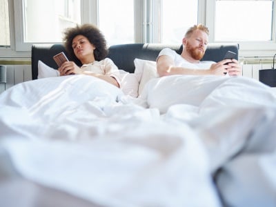 Ein Mann und eine Frau liegen mit ihren Handys im Bett und reden nicht miteinander.