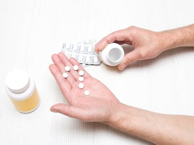 Fragezeichen, ges&auml;umt von wei&szlig;en runden Pillen in der Handfl&auml;che eines Mannes