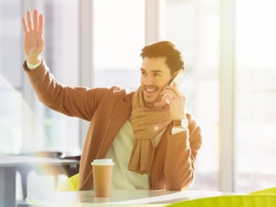 Ein lächelnder Mann, der in einem Café sitzt und mit der Hand winkt