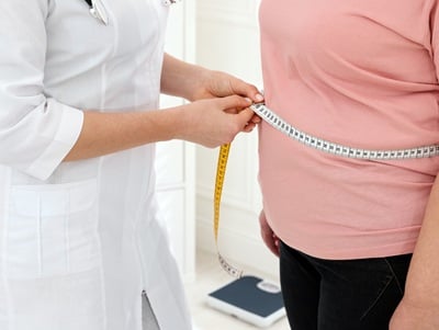 Ein Ernährungsberater misst den Taillenumfang einer übergewichtigen Frau.