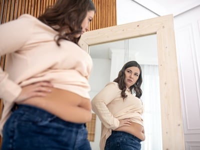 Eine &uuml;bergewichtige Frau betrachtet sich im Spiegel 