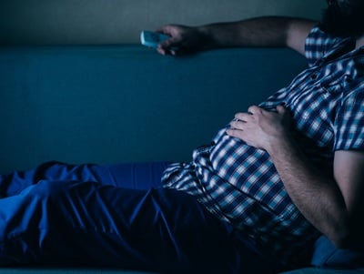 Ein übergewichtiger Mann mit einer Fernbedienung auf der Couch