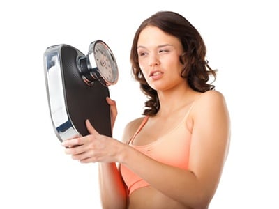 Eine junge Frau, die wütend auf die Waage schaut