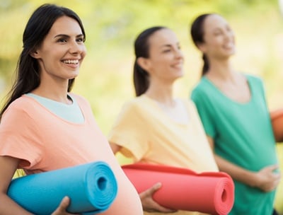 Drei schwangere Frauen bereiten sich freudig auf eine Yogastunde im Freien vor