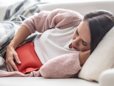 Eine Frau liegt mit Unterleibsschmerzen auf dem Sofa