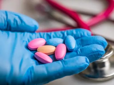A gloved healthcare professional holds colorful medications