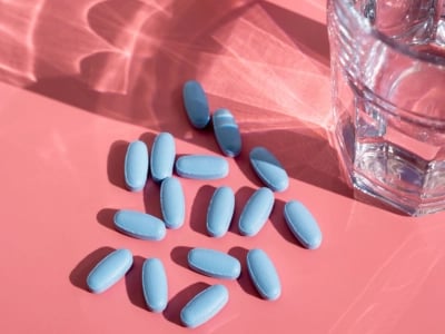 Blaue Tabletten neben einem Glas Wasser auf rosa Hintergrund