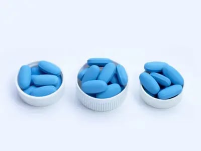 Blue Viagra tablets placed in small white caps on a light background