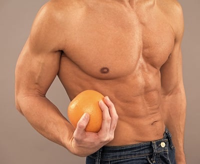 Fitter Mann mit muskulösem Oberkörper hält Orangen als Diät-Symbol