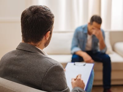 Ein trauriger Mann sitzt auf der Couch, während ein Psychologe Notizen macht